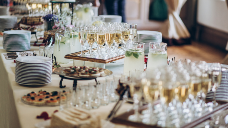 Ein dekorativ aufgebautes Buffet mit Champagnergläsern, Fingerfood-Häppchen und Tellern.